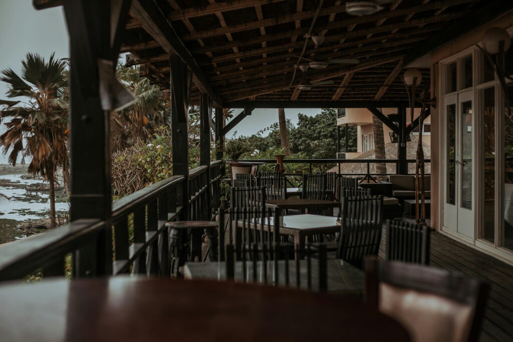 An idyllic seaside patio with empty wooden chairs, surrounded by lush tropical foliage.