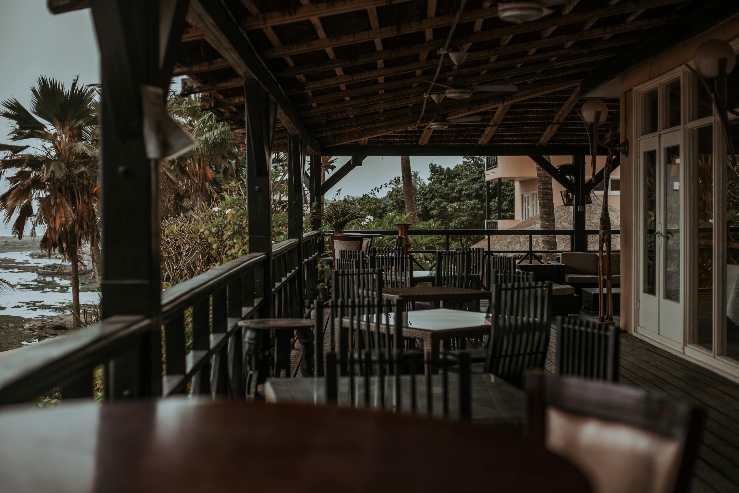 An idyllic seaside patio with empty wooden chairs, surrounded by lush tropical foliage.